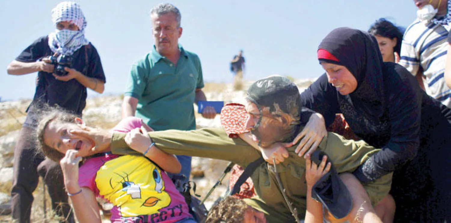 جندي إسرائيلي يحاول اعتقال شابة فلسطينية خلال المواجهات التي اندلعت أمس بين الجانبين بالقرب من رام الله (رويترز)