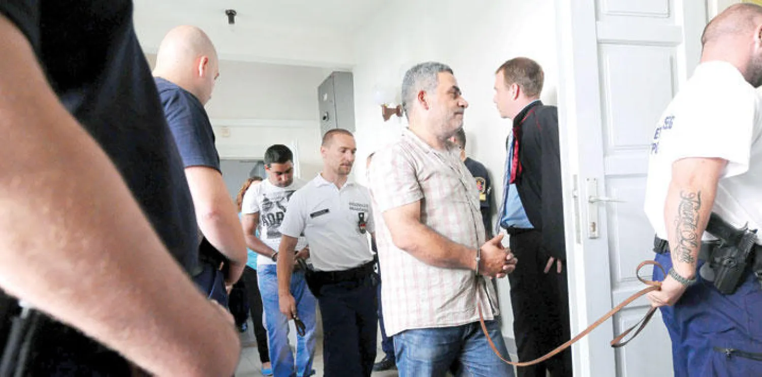 أحد المشتبه بهم الأربعة في قضية «شاحنة الدواجن» يقتاده أمس شرطي مجري إلى محكمة مدينة كيسكيميت الواقعة بين بودابست والحدود الصربية (أ.ف.ب)