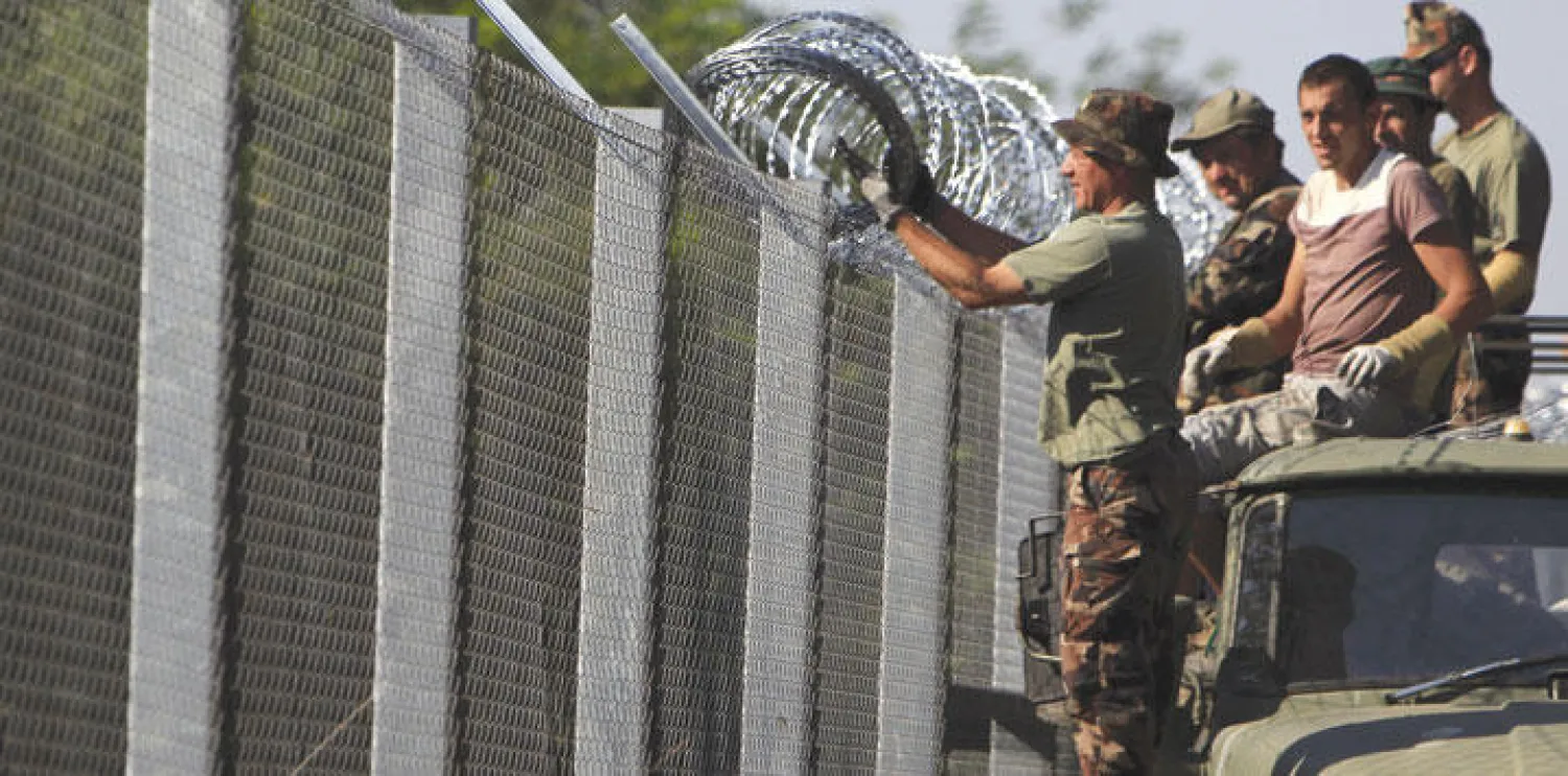 جنود مجريون يضبطون الأسلاك الشائكة فوق سور على الحدود لمنع تدفق اللاجئين الذين يشكل السوريون غالبيتهم (رويترز)