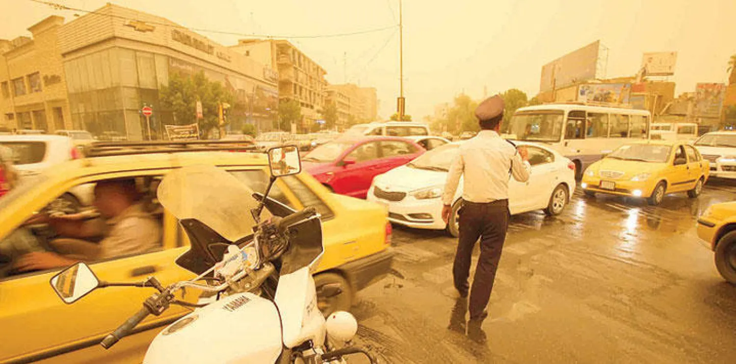 شرطي مرور ينظم حركة السير في أحد شوارع بغداد خلال عاصفة ترابية أمس (أ.ف.ب)