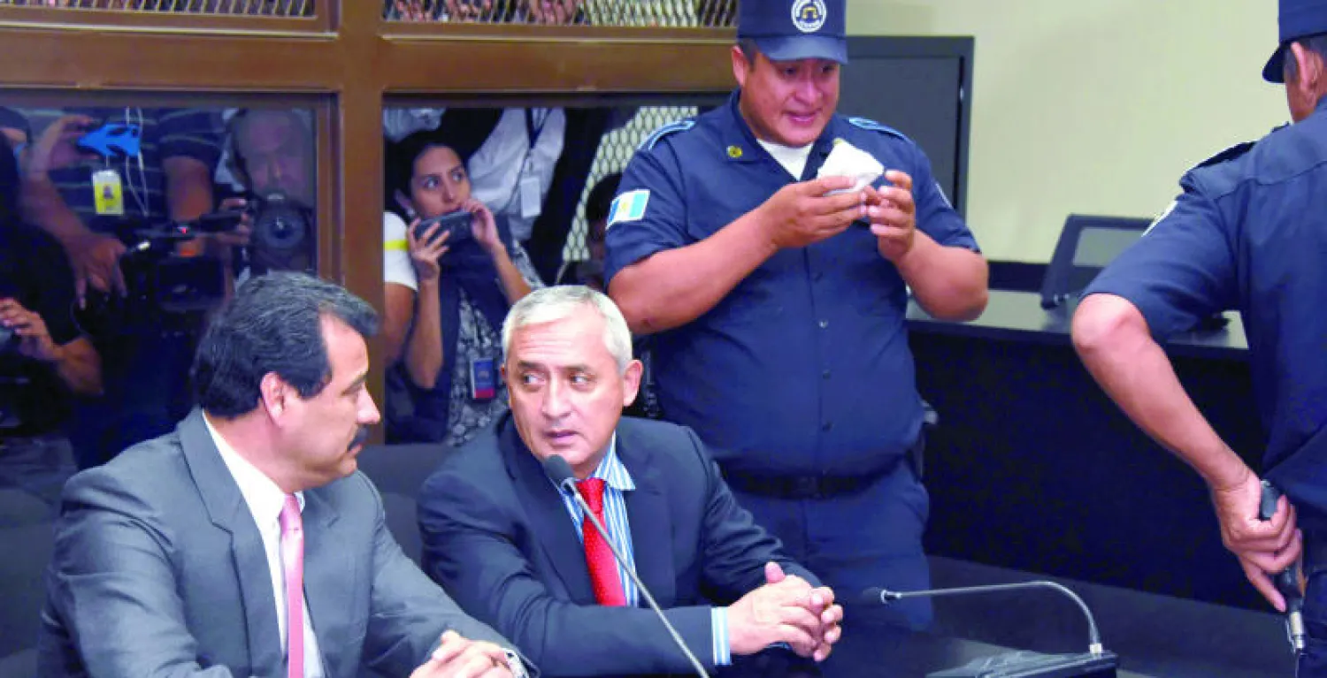 الرئيس المستقيل أوتو بيريز يتحدث مع محاميه خلال مثوله أمس أمام المحكمة لمواجهة الاتهامات الموجهة إليه (أ.ف.ب)