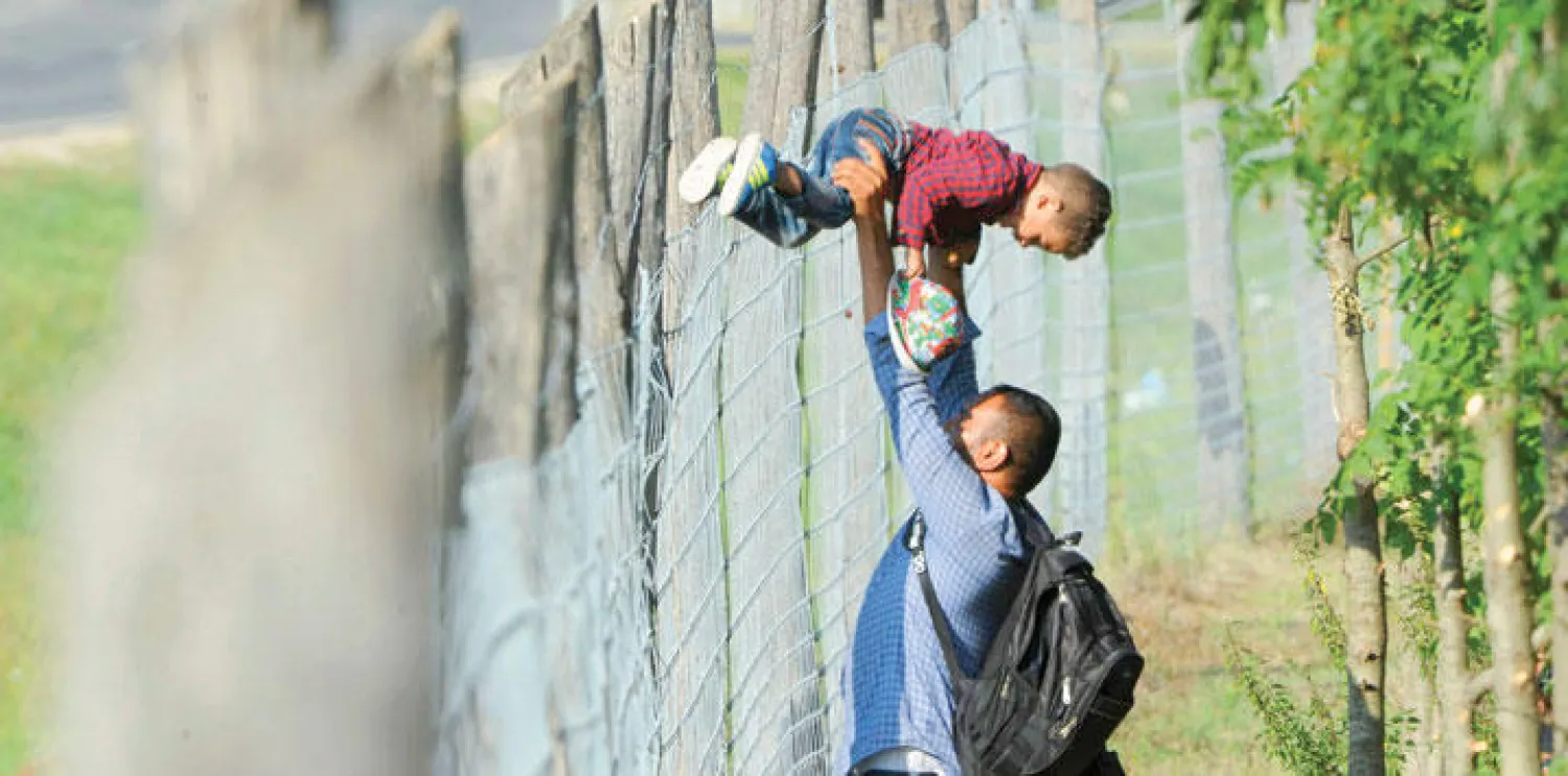 مهاجر يساعد ابنه على اجتياز سياج مركز لاستقبال اللاجئين في بلدة روسكي  بهنغاريا أمس (رويترز)