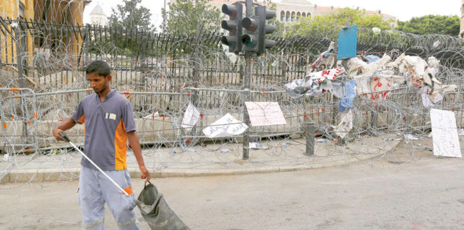 عامل ينظف الشارع قرب مقر الحكومة اللبنانية المحاط بالأسلاك الشائكة في العاصمة بيروت أمس (رويترز)