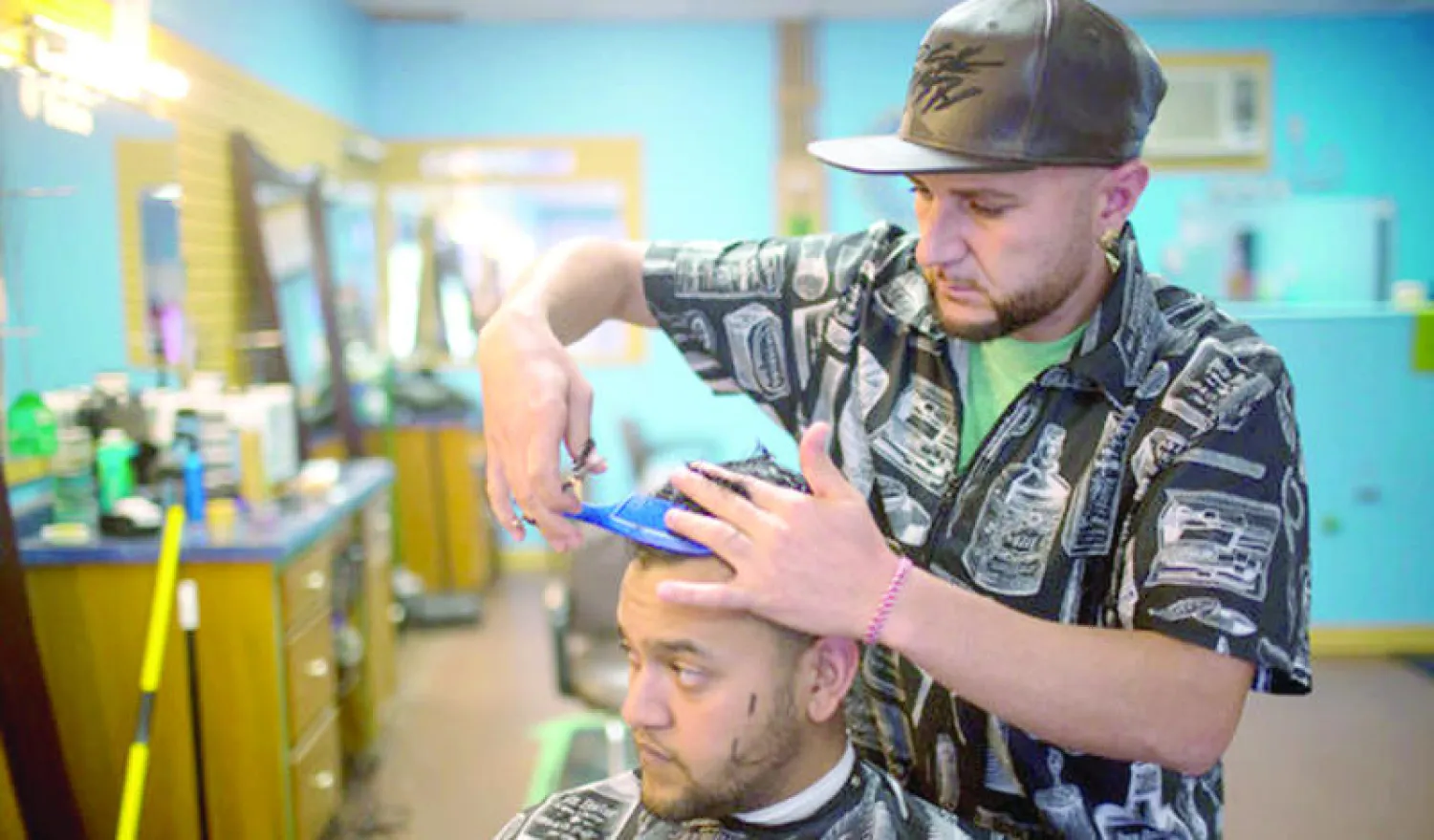 الإيزيدي حسن خليل يحلق شعر زبون في صالونه بنبراسكا (نيويورك تايمز)