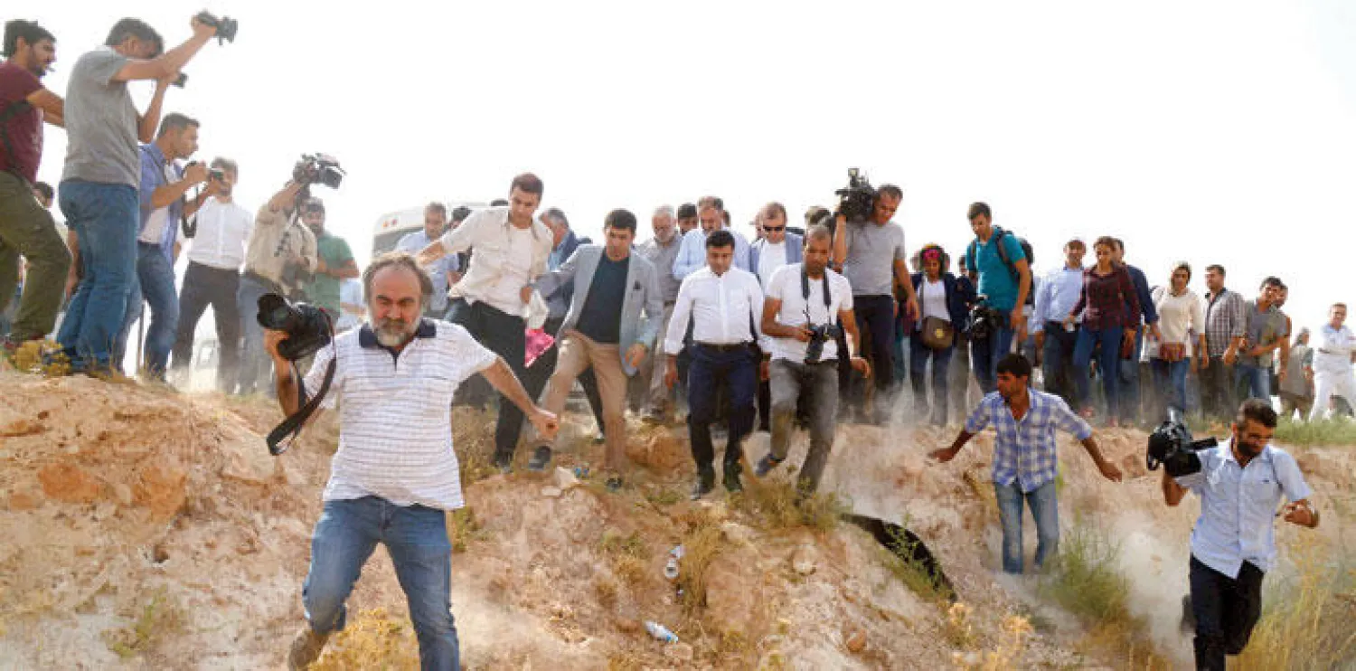 صلاح الدين دمرتاش زعيم حزب الشعوب الديمقراطي المؤيد للأكراد في تركيا لدى عبوره أحد الحقول مع وسائل الإعلام بعد أن منعته السلطات من التوجه بالسيارة إلى بلدة جزيرة (أ.ف.ب)