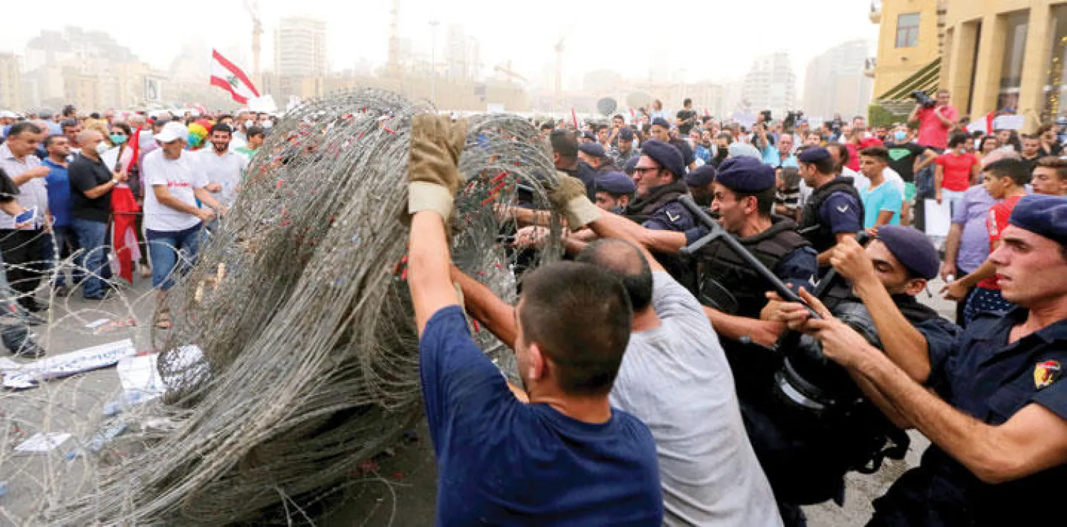 ناشطون لبنانيون يساعدون عناصر من الشرطة في إزالة أسلاك شائكة كانت تحول دون الوصول إلى مبنى البرلمان في بيروت أمس (إ.ب.أ)