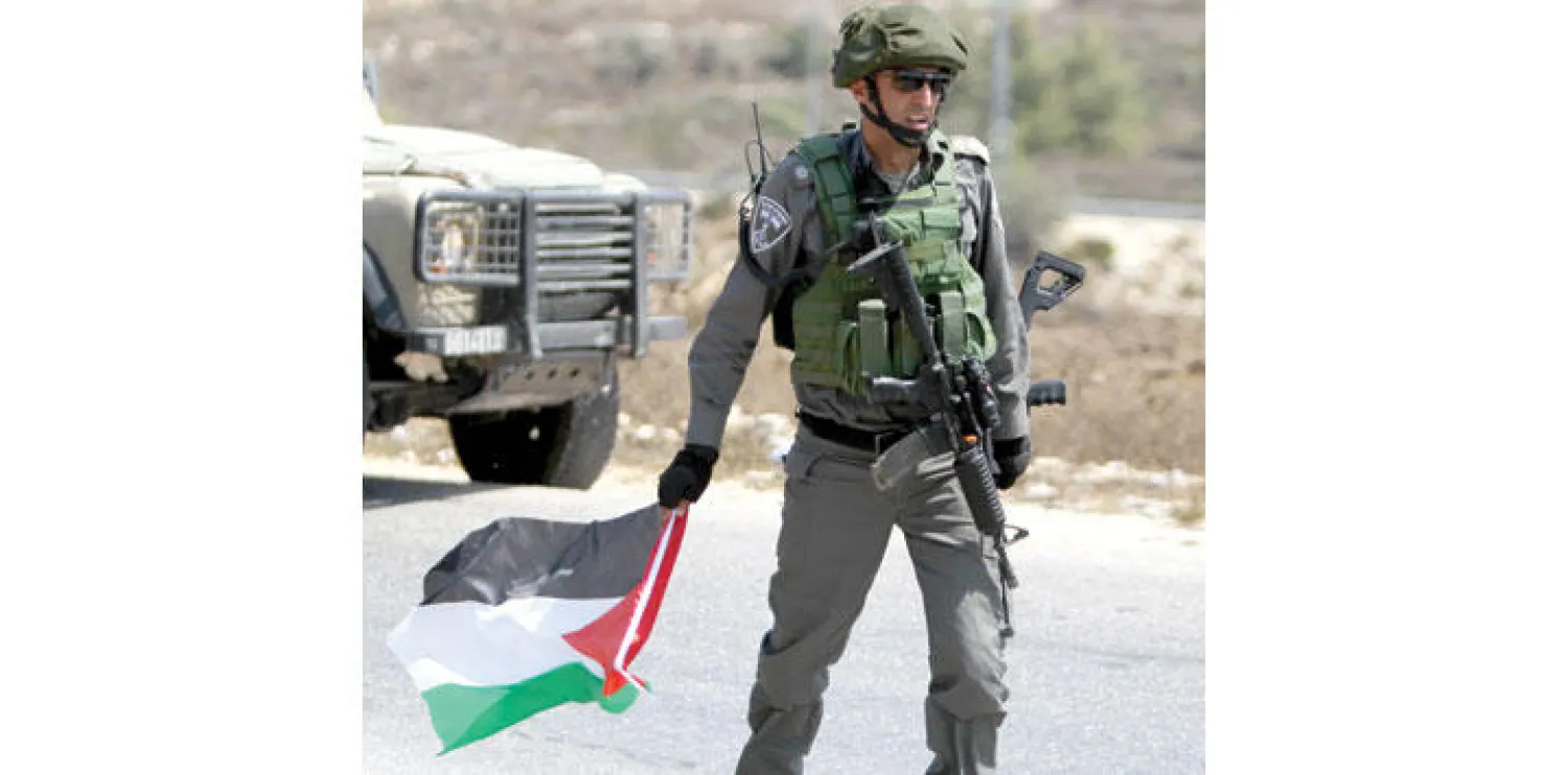 جندي إسرائيلي يحمل العلم الفلسطيني بعد أن صادره من أحد الفلسطينيين خلال مواجهات في أعقاب مظاهرة ضد مصادرة الأراضي الفلسطينية لتوسيع مستوطنة حلميش اليهودية في قرية النبي صالح بالضفة الغربية أمس (أ.ف.ب)