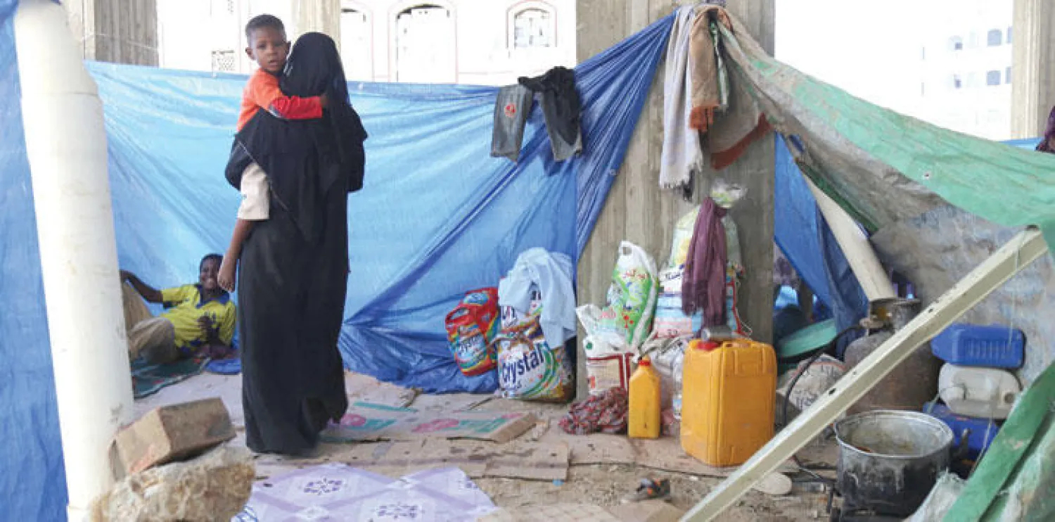 يمنية تحمل صغيرها في مكان عام اختارته كـ{خيمة} في مدينة تعز أمس بعدما نزحت مع كثيرين من منازلهم بسبب الحرب (أ.ف.ب)