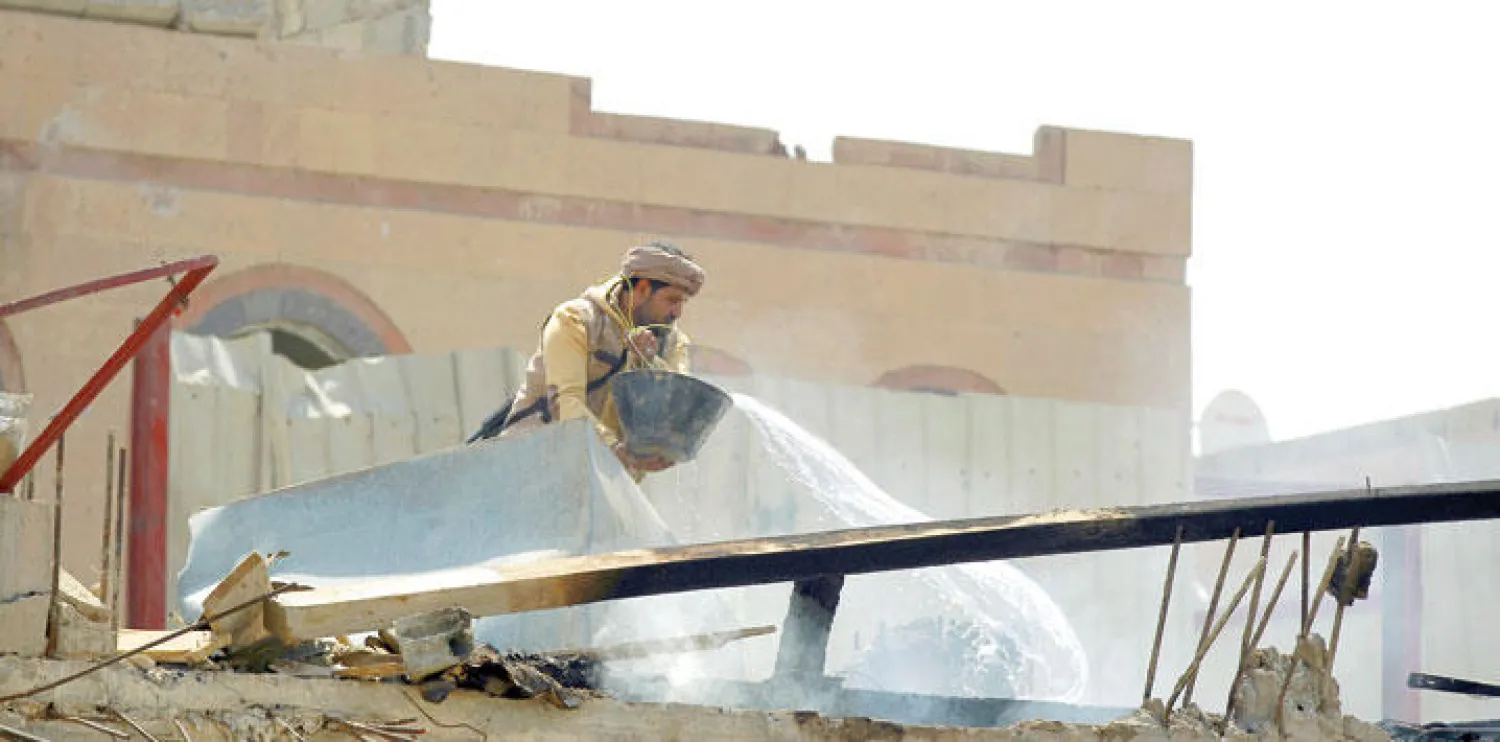 أحد أفراد ميليشيا الحوثي يصب الماء لإخماد أعمدة الدخان المتصاعدة من داخل أنقاض مبانٍ عسكرية دمّرتها الغارات الجوية لقوات التحالف في العاصمة صنعاء أمس (أ.ف.ب)