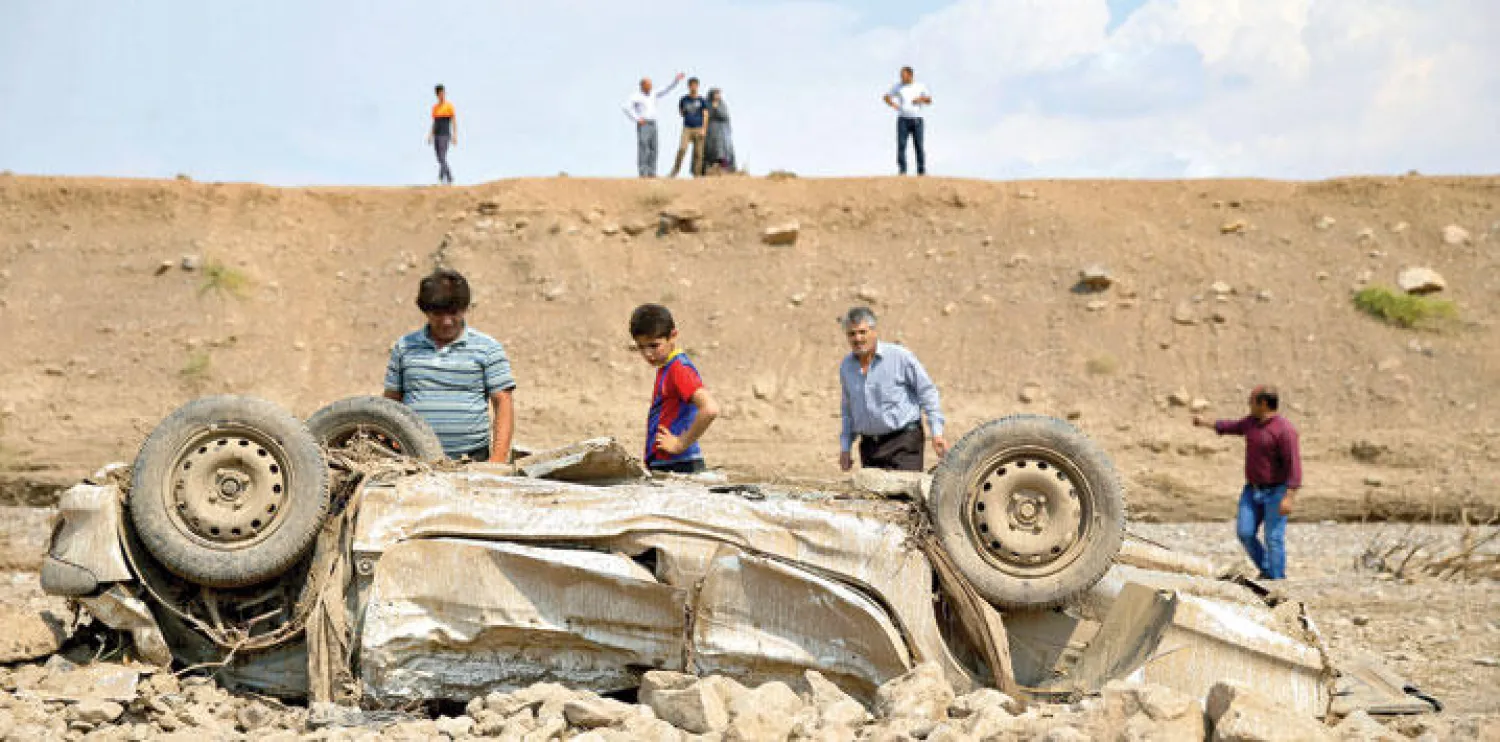 إيرانيون ينظرون إلى حطام سيارة جرفتها السيول في منطقة «باكدشت»، جنوب شرقي العاصمة طهران، أمس (أ.ب)