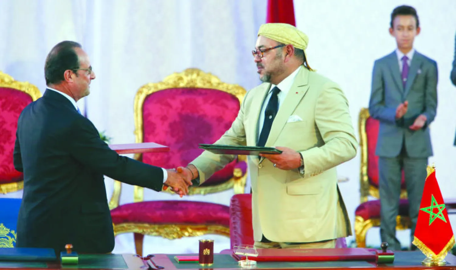 العاهل المغربي الملك محمد السادس والرئيس الفرنسي فرنسوا هولاند يتصافحان بعد توقيع اتفاقية بين البلدينفي طنجة أمس وبدا ولي العهد المغربي مولاي الحسن (أ.ب)