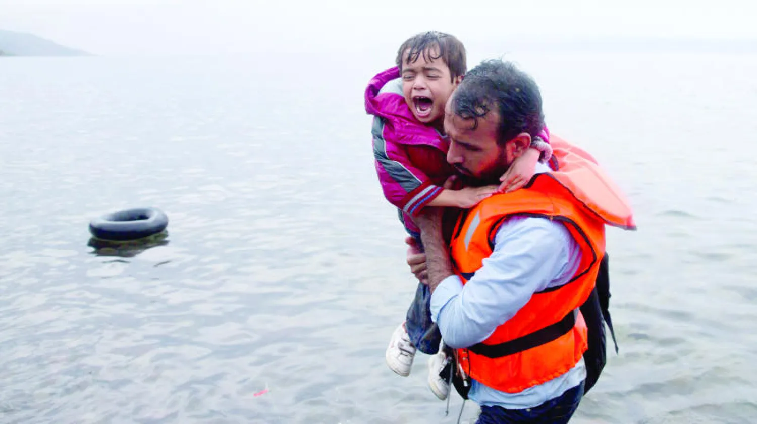 مهاجر يحمل طفلاً يبكي بعد وصولهما برفقة مجموعة مهاجرين آخرين إلى جزيرة ليزبوس اليونانية أمس (أ.ب)