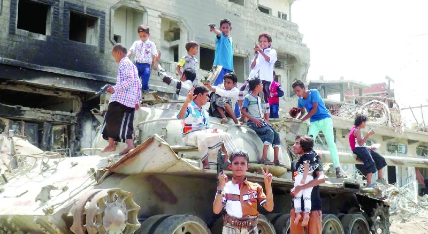 أطفال يمنيون يعتلون دبابة وهم يحملون ألعابًا تحاكي أسلحة خلال احتفالهم بالعيد في أحد الشوارع الرئيسية بعدن (رويترز)