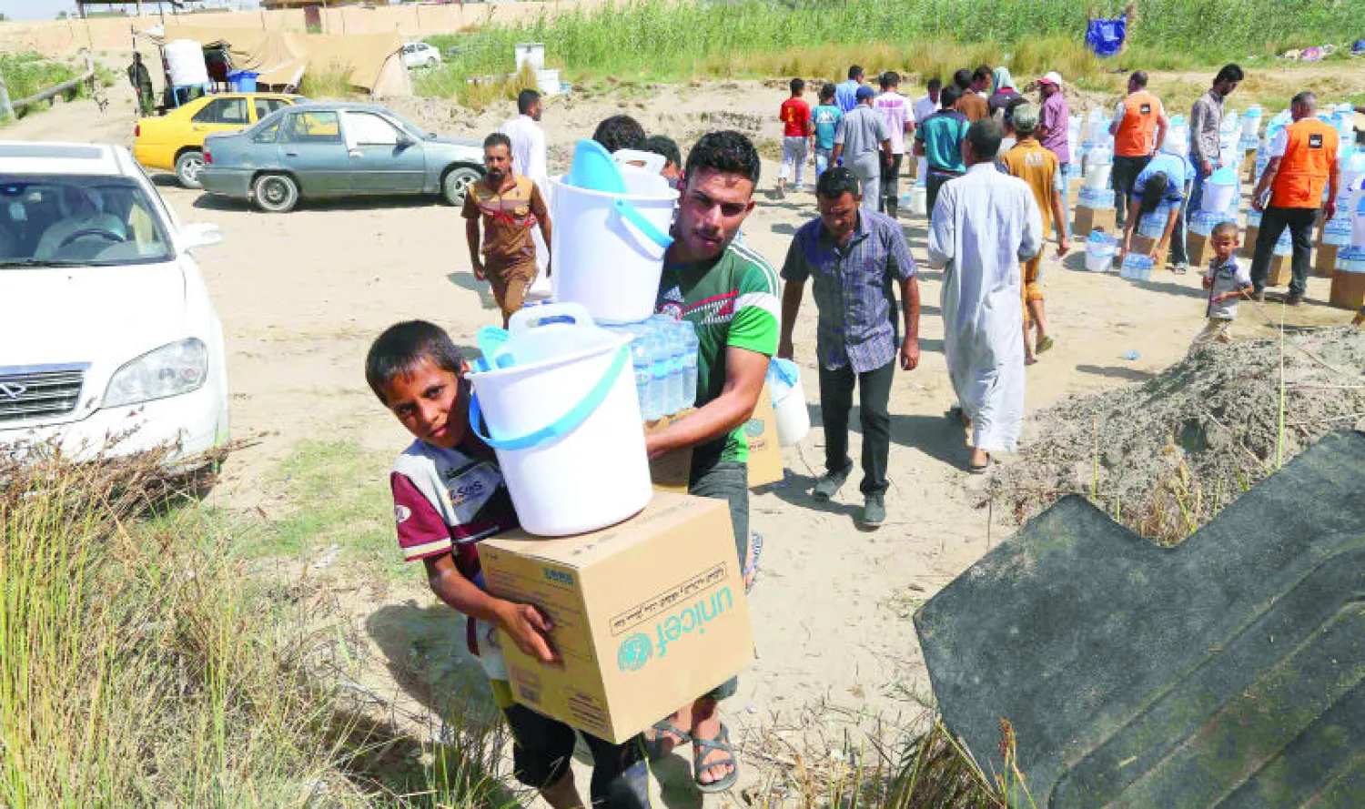 نازحون عراقيون يحملون مساعدات إنسانية وزعت عليهم عند «جسر بزيبز» غرب بغداد أمس (أ.ب)