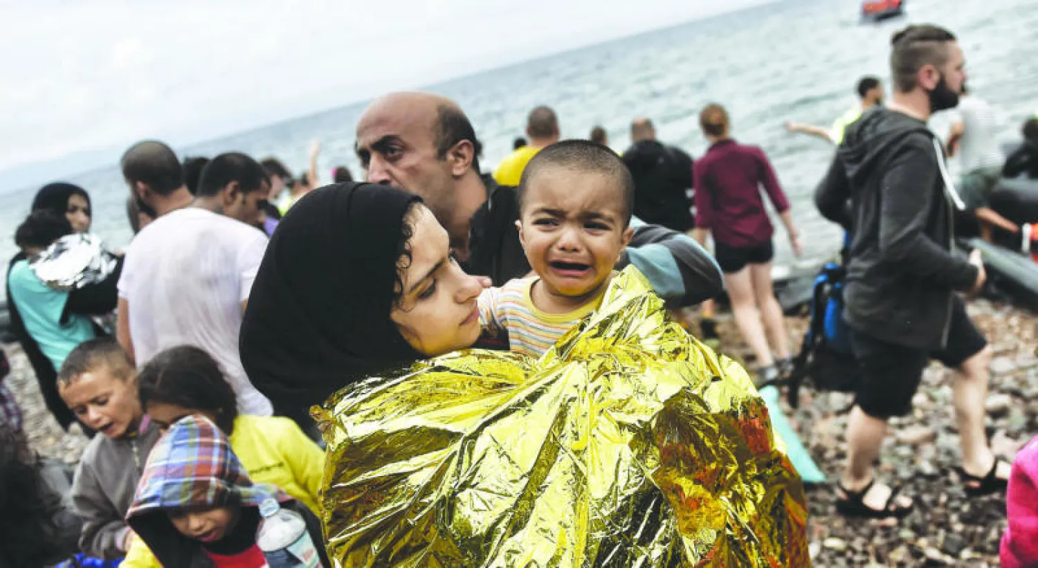 طفل سوري يبكي في حضن أمه بعد وصولهما، ومجموعة لاجئين سوريين، إلى جزيرة ليزبوس اليونانية أمس (أ. ف. ب)