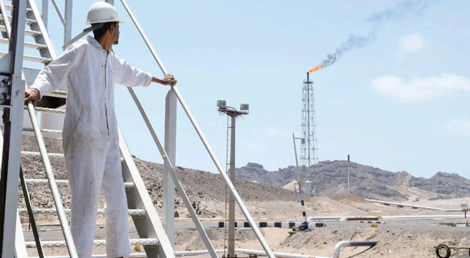 عامل ينظر إلى تصاعد الدخان مع استئناف العمل في مصفاة عدن للنفط أمس بعد توقف دام ستة أشهر (أ.ف.ب)