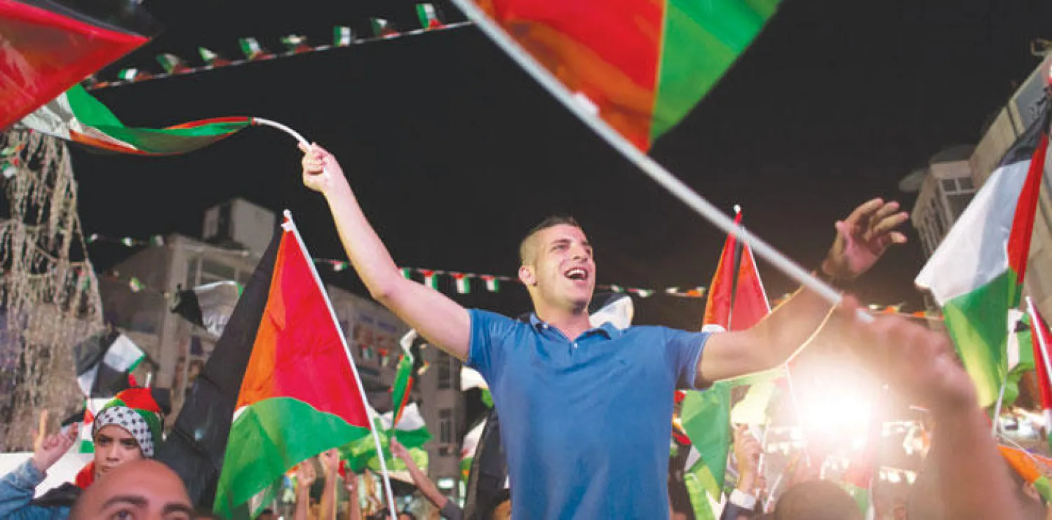 فلسطينيون في مدينة رام الله  بالضفة الغربية أمس ينشدون الأغاني الوطنية ويلوحون بالأعلام ابتهاجًا برفع العلم الفلسطيني على مبنى الأمم المتحدة بنيويورك (أ.ب)