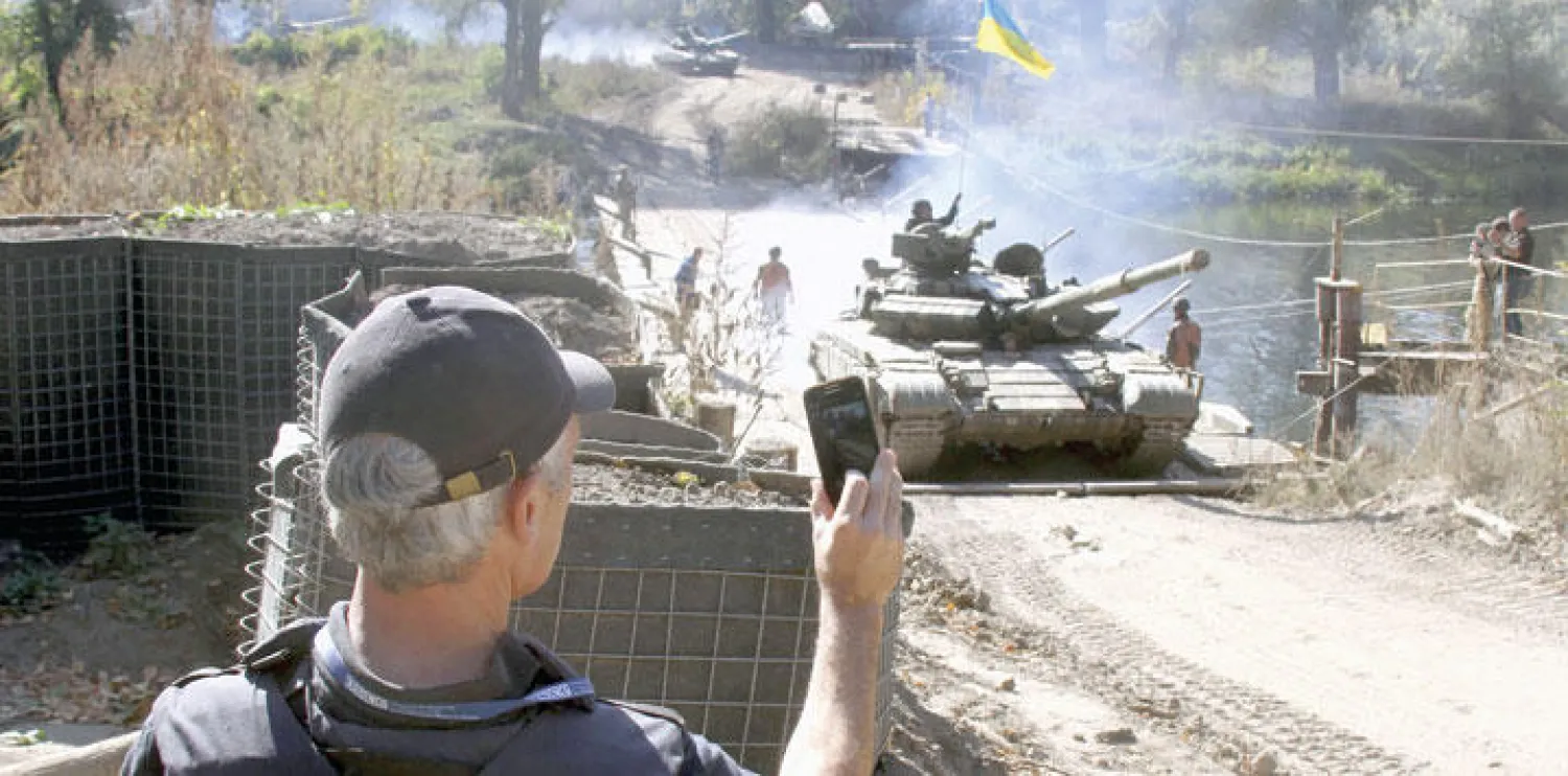 شرطي من القوات الدولية يراقب عملية سحب الدبابات بالقرب من بلدة نيزينجي شرق أوكرانيا أول من أمس (رويترز)