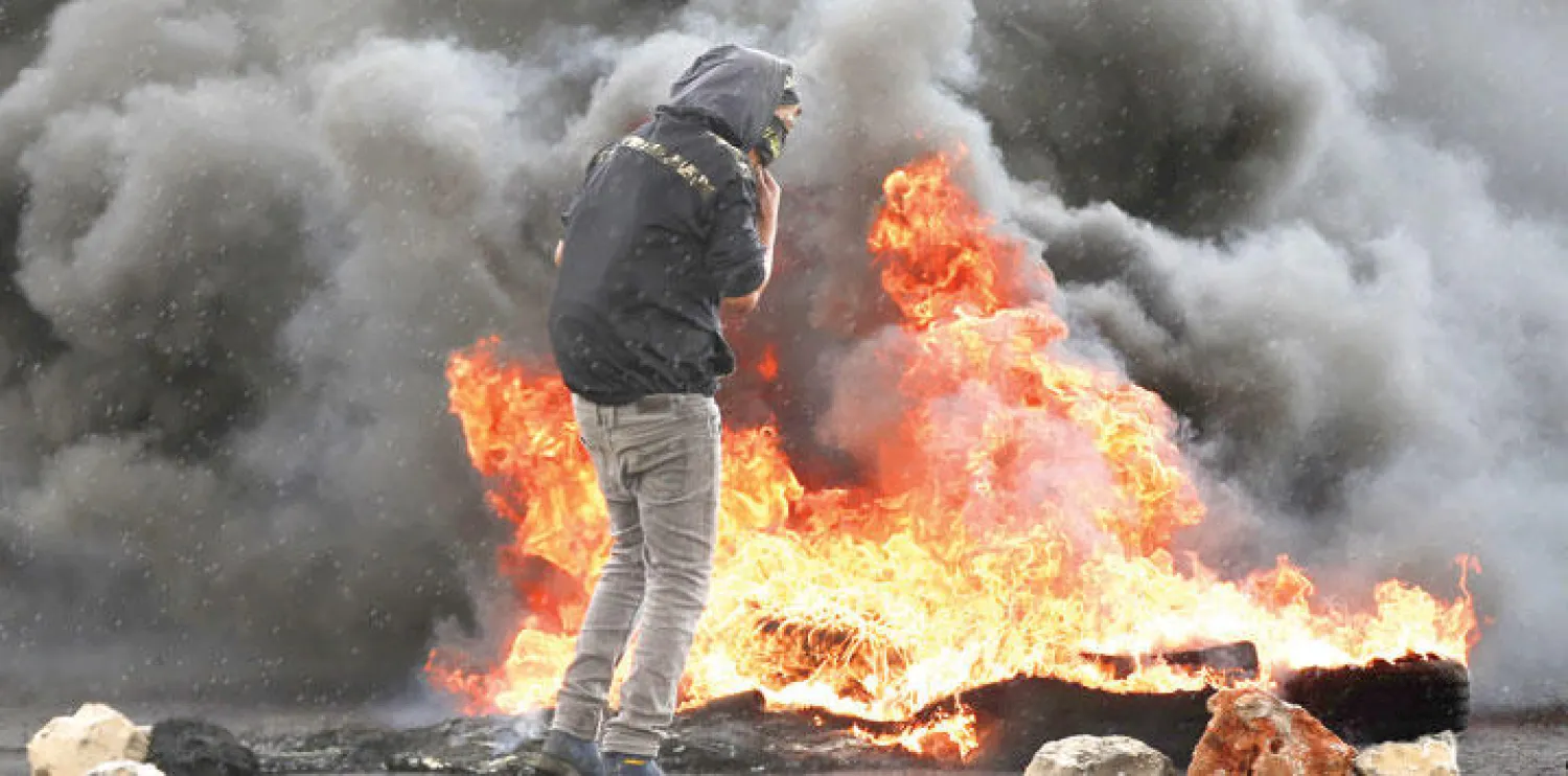 فلسطيني يقف بالقرب من إطارات محترقة خلال المواجهات التي وقعت أمس بين فلسطينيين وقوات الاحتلال الإسرائيلي قرب رام الله (أ.ف.ب)