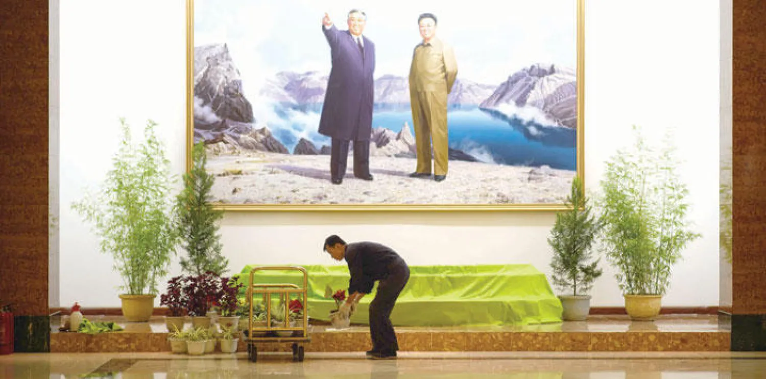 عامل يضع الزهور بجانب صورة زعيم كوريا الشمالية عشية احتفالات البلاد بالذكرى الـ 70 لتأسيس حزب العمال الحاكم والوحيد (أ.ف.ب)