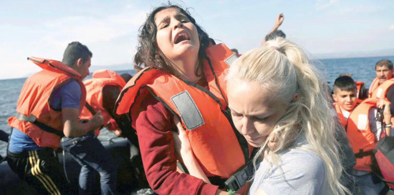 ناشطة في إحدى الجزر اليونانية تحمل طفلة سورية لاجئة بعد وصول قارب يحمل العشرات من تركيا (إ.ب.أ)