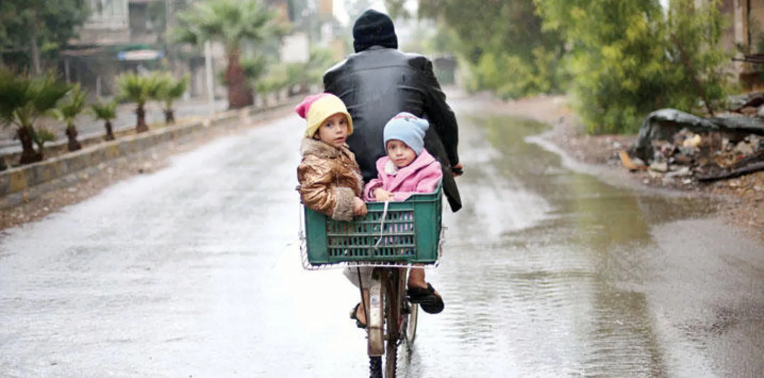 مواطن سوري يستقل دراجته الهوائية ناقلاً معه طفلتيه في ضاحية كفر بطنا التي تسيطر عليها قوات المعارضة بالغوطة الشرقية قرب العاصمة السورية دمشق (أ.ف.ب)