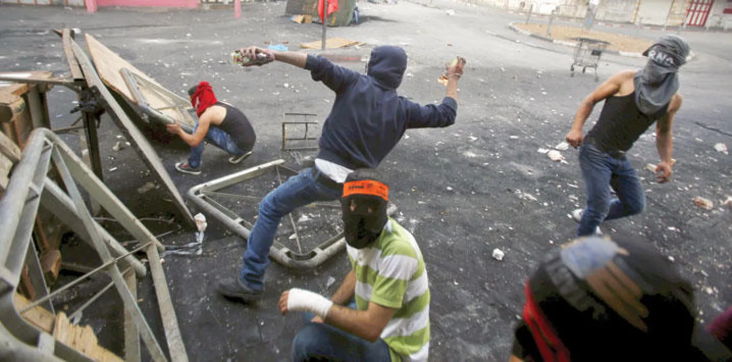 ملثمون فلسطينيون يرجمون قوات الاحتلال في مدينة الخليل أمس (رويترز)