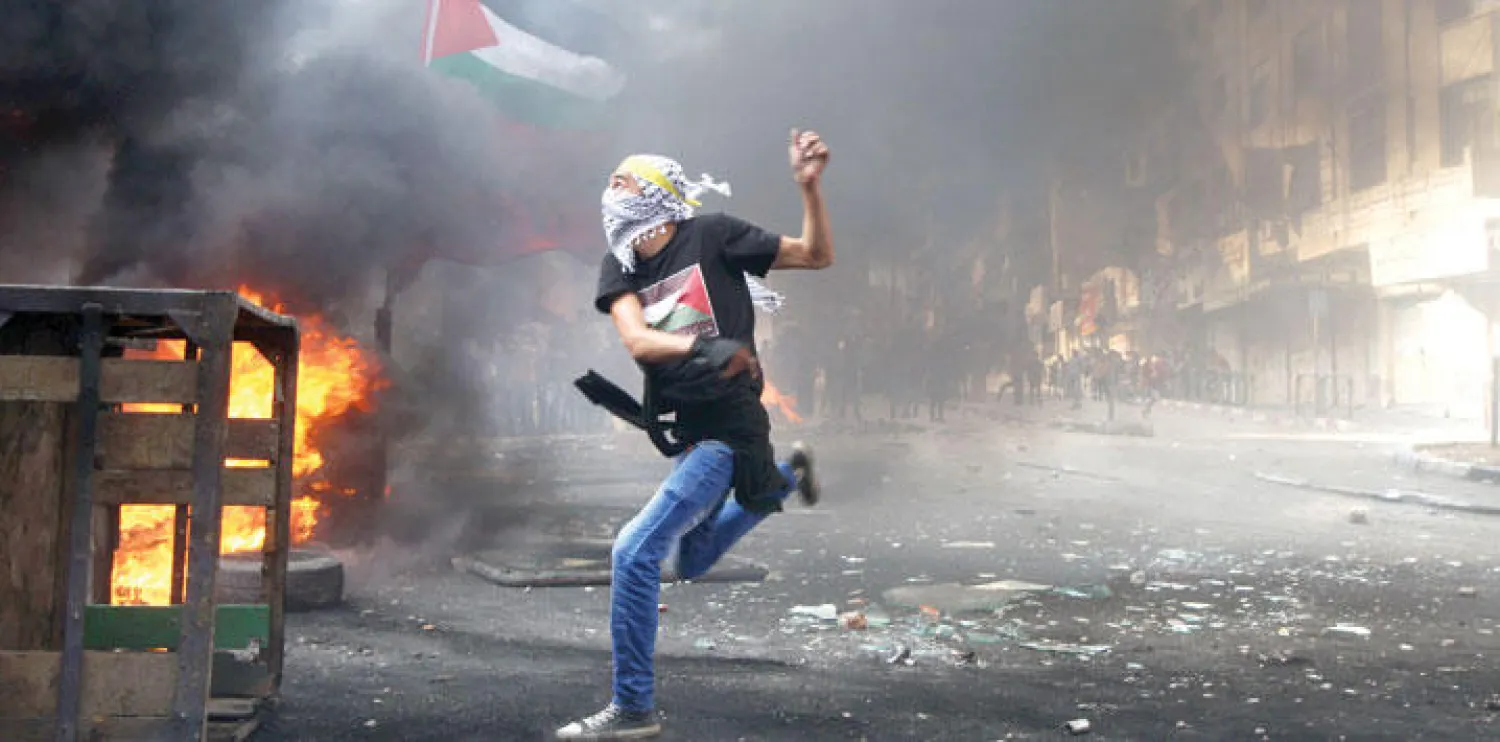 شاب فلسطيني ملثم يلقي بالحجارة على جنود إسرائيليين في الضفة الغربية أمس (أ.ف.ب)