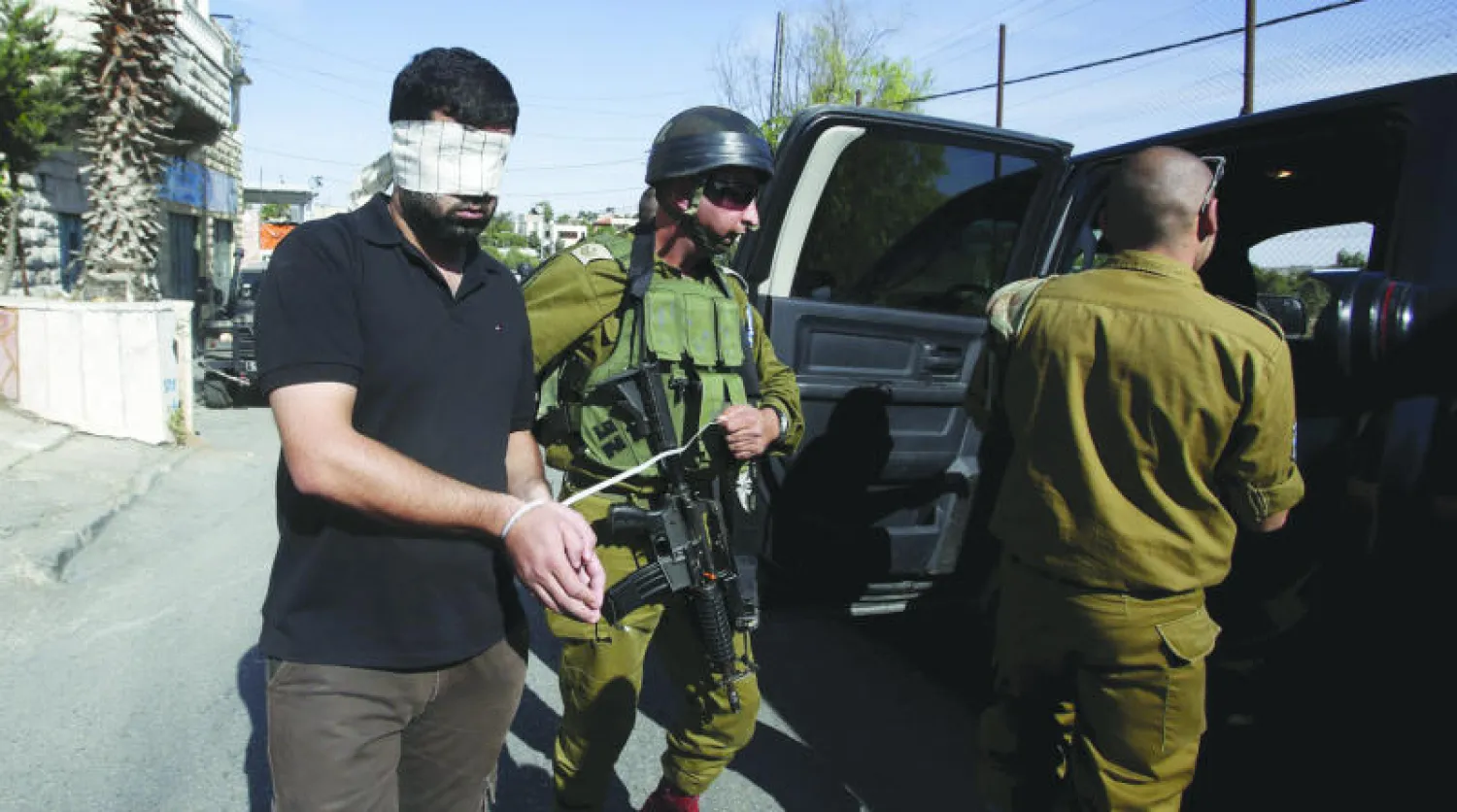 جنود إسرائيليون يعتقلون فلسطينيًا معصوب العينين في مدينة الخليل أمس (رويترز)