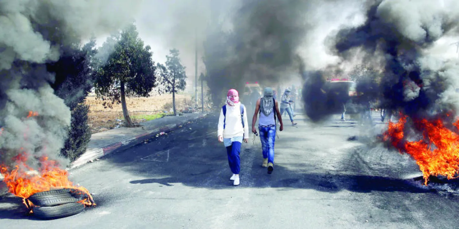 شبان فلسطينيون يمشون وسط إطارات مشتعلة خلال مواجهات مع قوات الاحتلال قرب مستوطنة بيت إيل على أطراف رام الله بالضفة الغربية أمس (أ.ف.ب)