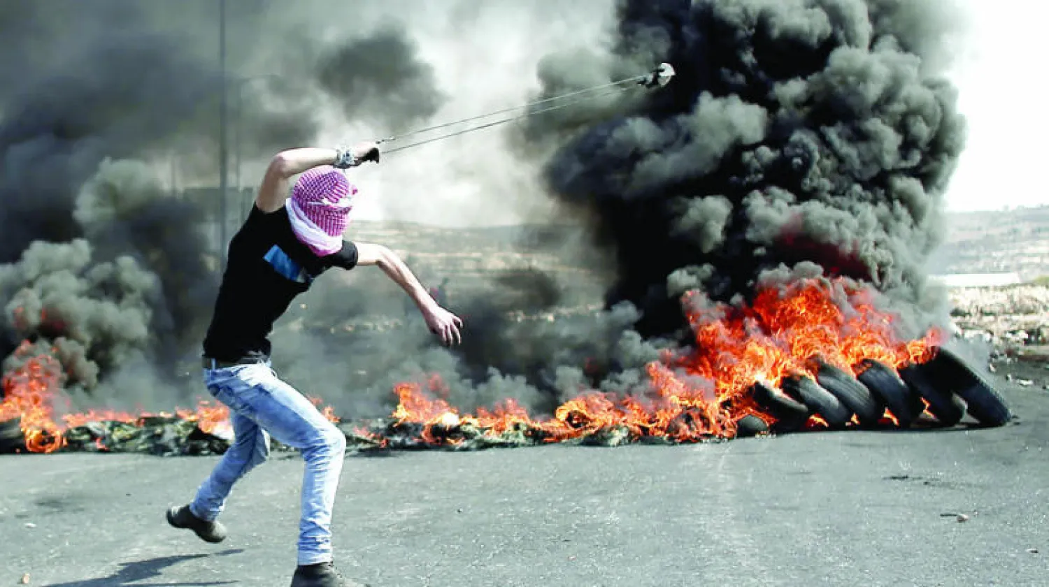 فلسطيني يستخدم مقلاعاً لرمي الحجارة على جنود إسرائيليين في مدينة البيرة برام الله أمس (ا.ف.ب)