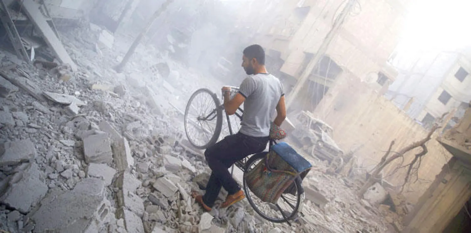 شاب من بلدة دوما شرق العاصمة السورية يعبر بدراجته أمس أنقاض المباني التي تعرضت للدمار بعد غارات لطيران النظام (أ.ف.ب)