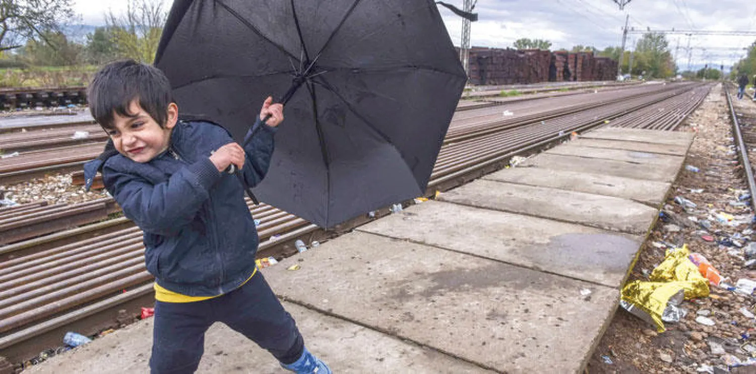 طفل مهاجر يحمل مظلة في محطة قطار بعد أن عبر ومهاجرون آخرون الحدود المقدونية - الصربية أمس (أ.ف.ب)