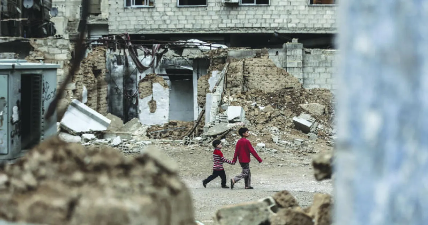 طفلان سوريان من بلدة دوما بريف دمشق يعبران المباني المدمرة بفعل قصف الطيران الحربي (إ.ب.أ)