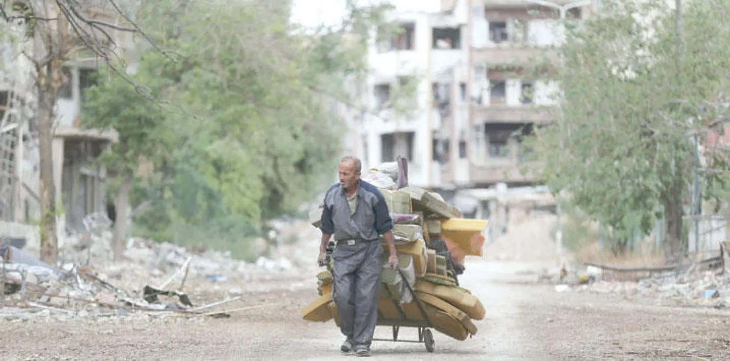رجل يجر عربة محملة بالفرش مخترقًا المنطقة المدمرة بفعل طيران النظام في حي جوبر قرب دمشق (رويترز)