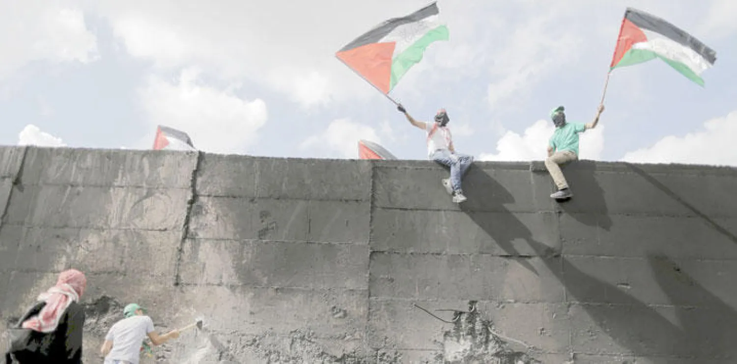 متظاهر فلسطيني يحاول إحداث فتحة في الجدار الفاصل، على وقع المواجهات مع الجنود الإسرائيليين في قرية أبوديس شرق القدس أمس (رويترز) (تفاصيل ص8)