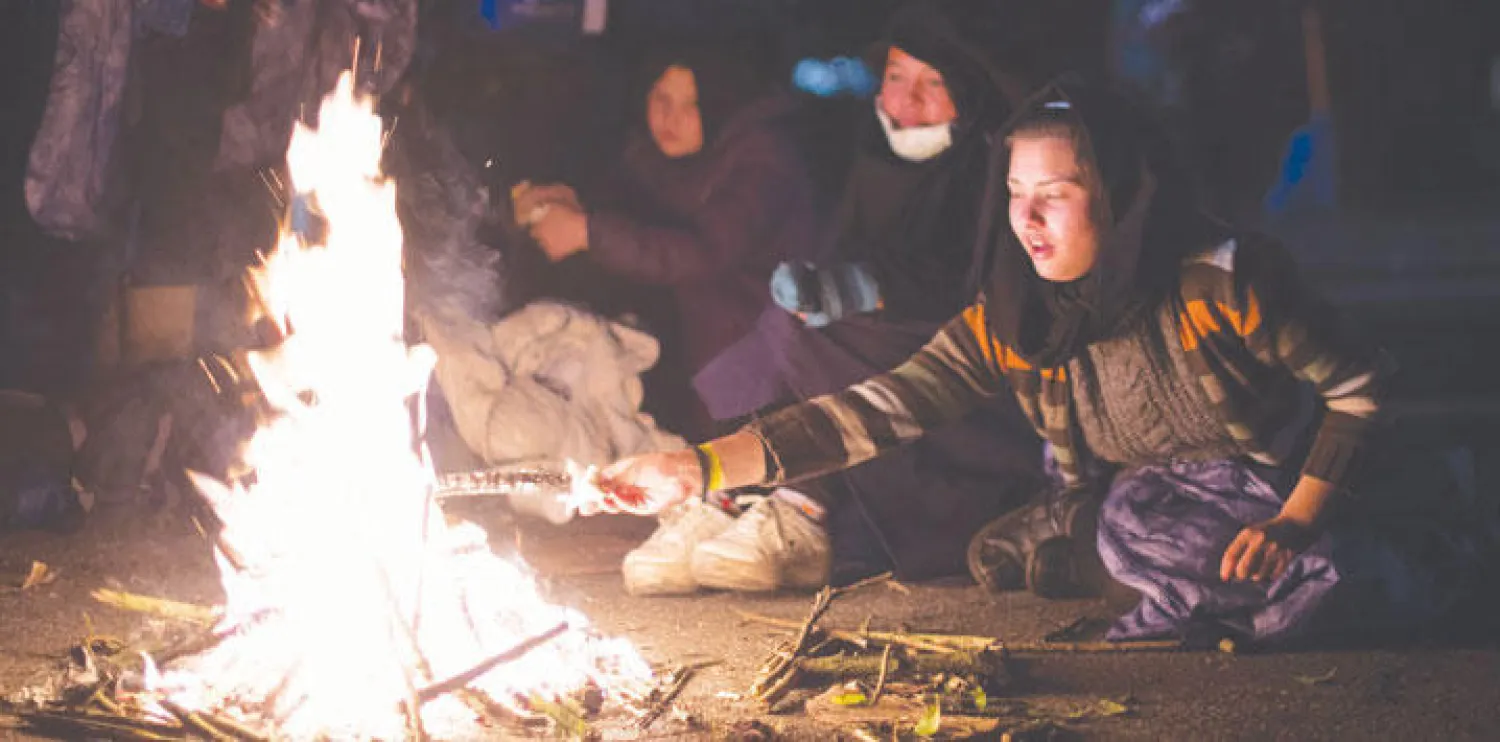 مهاجرات يشعلن النار بالقرب من مدينة باساو الألمانية، أول من أمس، بانتظار الحافلات التي ستنقل طالبي اللجوء إلى الملاجئ المعدة لهم رسميًا (أ.ب)