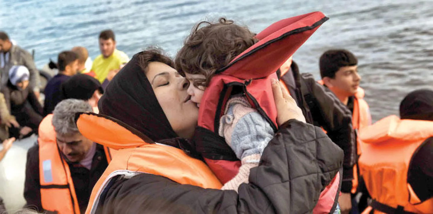أمّ تقبل طفلها بعد أن وصلت بسلام مع مجموعة مهاجرين آخرين إلى جزيرة ليسبوس اليونانية أمس (أ.ف.ب)