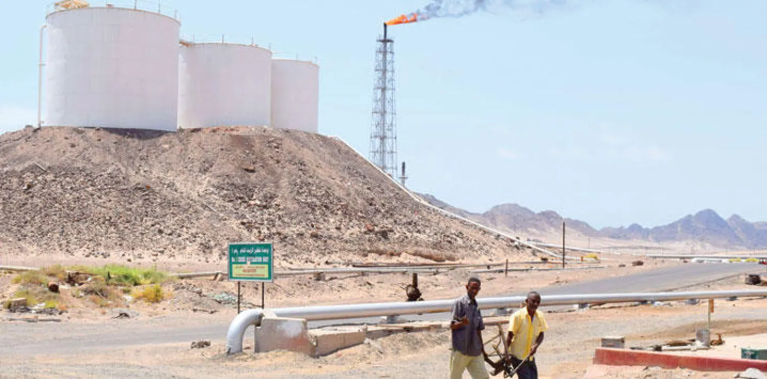 عاملان يمنيان يسيران بمحاذاة مصفاة النفط بمدينة عدن الجنوبية (أ.ف.ب)