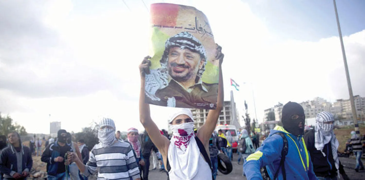 متظاهر فلسطيني يرفع عاليا ملصقا لياسر عرفات خلال اشتباكات مع قوات الاحتلال في الذكرى 11 لرحيله (أ.ب)