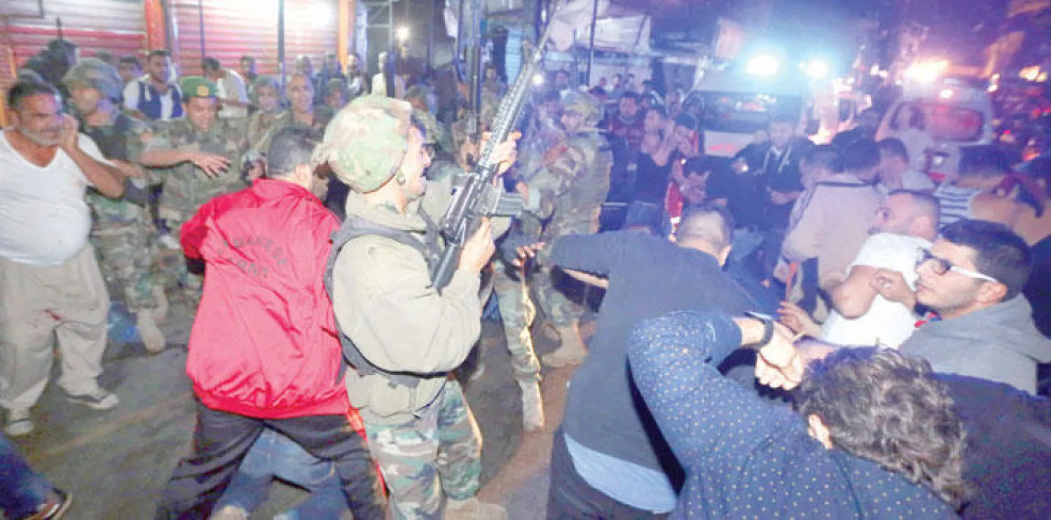 عسكري من الجيش اللبناني يطلق النار في الهواء لتفريق المتجمعين بمكان التفجيرين في الضاحية الجنوبية لبيروت (أ.ب)