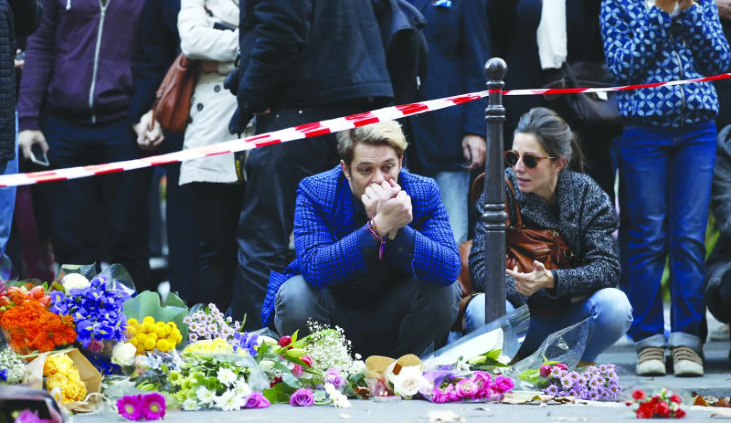 فرنسيان يعبران عن حزنهما واستيائهما في العاصمة باريس ويقدمان باقات الورود لضحايا هجمات باريس أمس (أ. ف. ب)