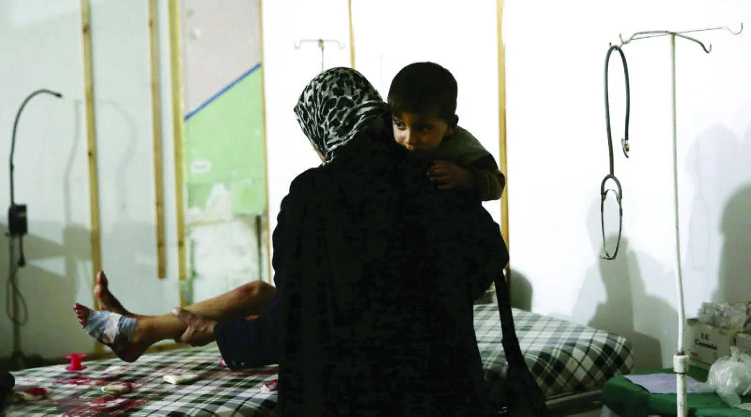 امرأة من مدينة دوما بريف دمشق تحمل طفلها بينما تتابع علاج ابنها الآخر الجريح جراء قصف الطيران الحربي للمنطقة أمس (رويترز)