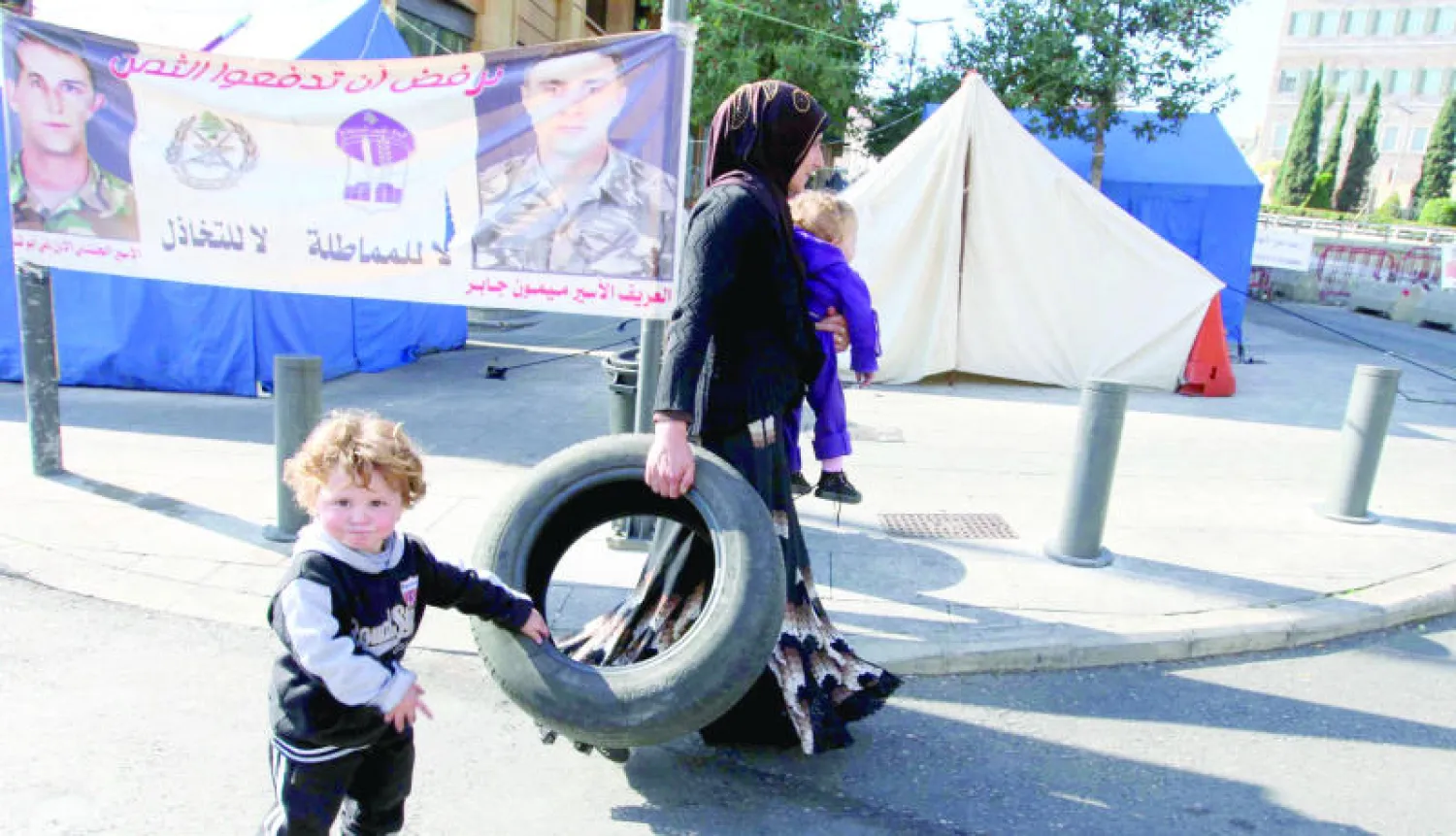 لبنانية تحمل مع طفلها أمس إطار سيارة لحرقه أمام مقر الحكومة في بيروت احتجاجا على اختطاف جنود لبنانيين في ديسمبر الماضي (غيتي)