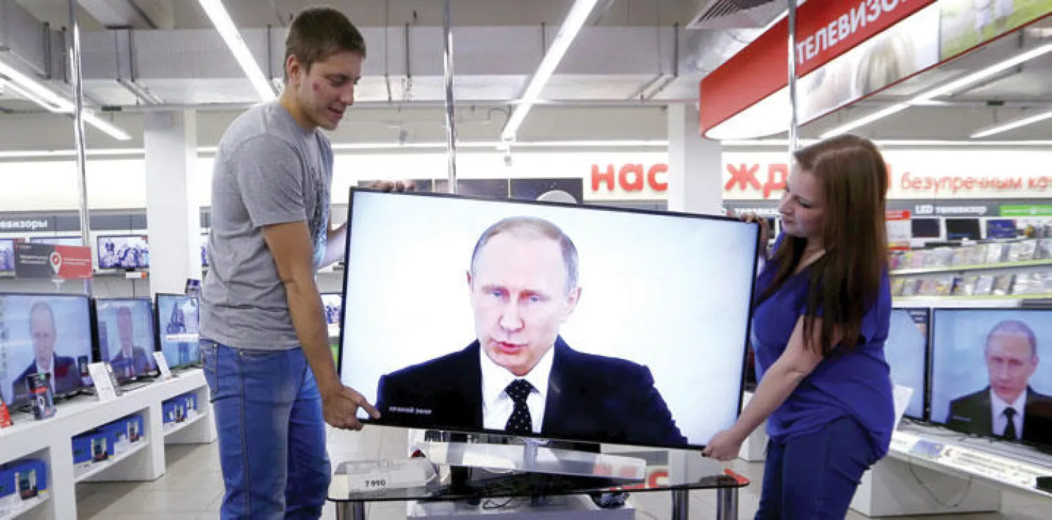 عاملان في متجر أدوات كهربائية في موسكو يحملان أمس جهاز تلفزيون يبدو على شاشته الرئيس الروسي بوتين (إ.ب.أ)