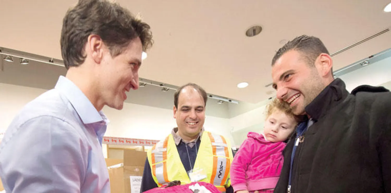 رئيس الوزراء الكندي في مطار تورونتو يحيي لاجئين وصلوا من سوريا ضمن قرار كندا استقبال عشرة آلاف سوري بنهاية هذا العام (إ.ب)