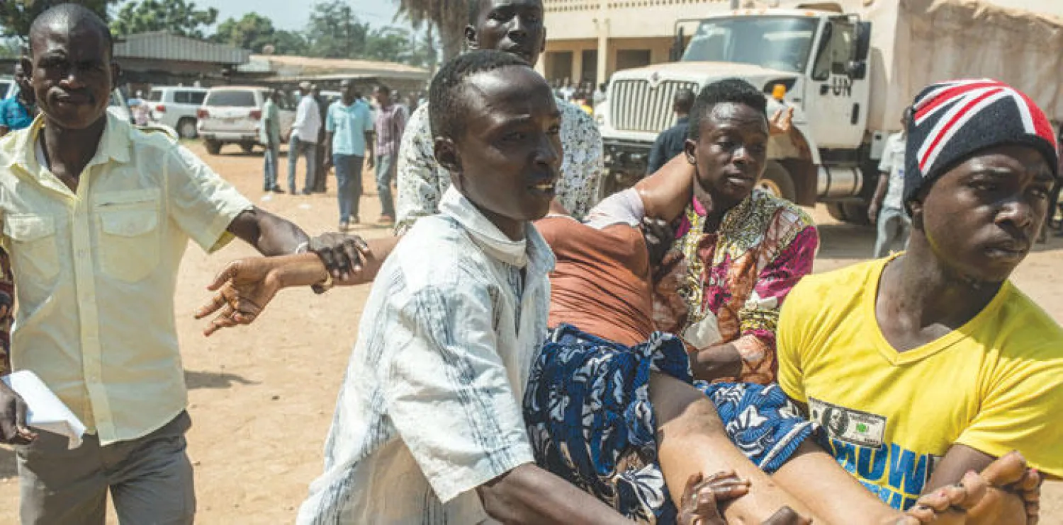 مواطنون يحملون امرأة أصيبت خلال تبادل إطلاق النار بين المؤيدين للاستفتاء ومعارضيه وسط العاصمة بانغي أمس (أ.ف.ب)