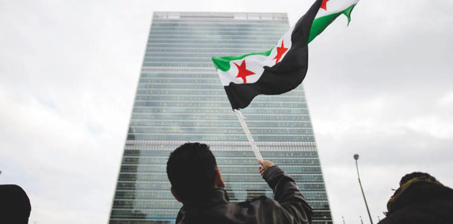 متظاهر سوري يرفع علم الثورة السورية أثناء انعقاد مجلس الأمن بخصوص سوريا (إ.ب.أ)