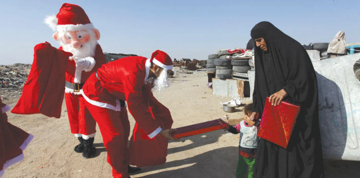 متطوعون يرتدون ملابس سانتا كلوز (بابا نويل) يقومون بتوزيع الهدايا على الأطفال في النجف جنوب بغداد أمس (رويترز)
