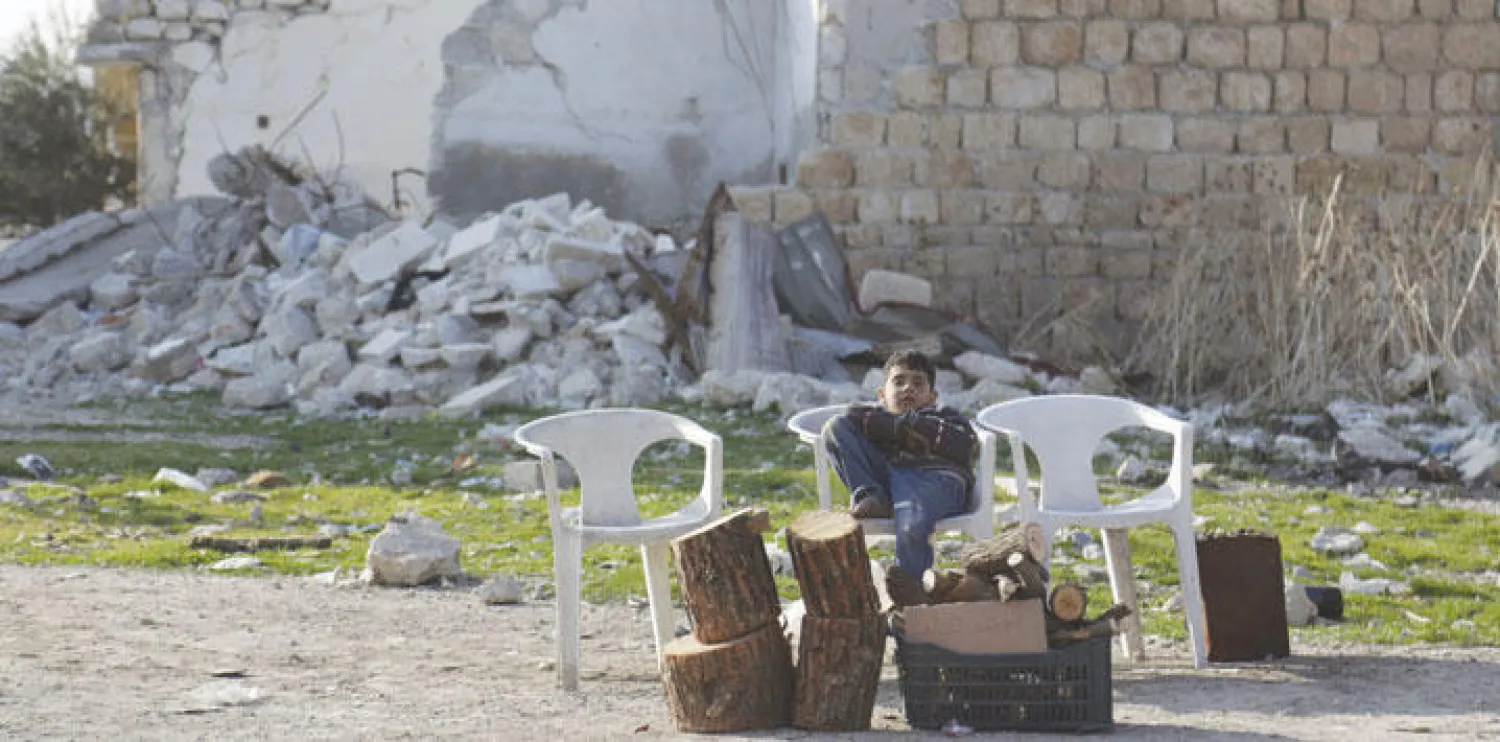 صبي يأخذ قسطا من الراحة أثناء بيعه أخشاب التدفئة في معرة النعمان بإدلب أمس (رويترز)